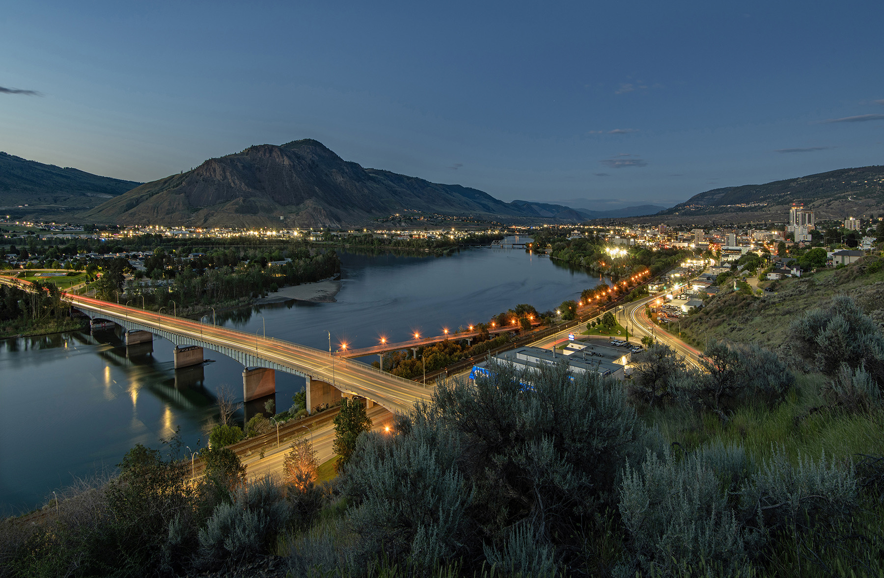 Kamloops at dusk — the bridge over the Thompson River, city lights, and Mount Peter and Paul beyond